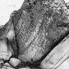 Black and white photo of large rock with words scratched deep on in its face