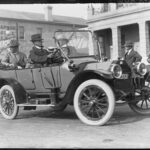 Image: Four men travel in an early twentieth-century car. A couple of buildings are visible in the background, including one with the words ‘Semaphore Coffee Palace’ painted on its side