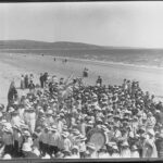 Image: Large group of children wearing hats on a beach with hills in the background