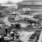 Image: a large demolition site with piles of rubble. The site is dotted with men in early 20th century clothing and horse drawn carts.