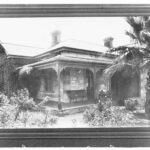 Image: A woman stands in a garden in front of a large, single-storey stone house