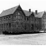 Image: large stone building with group of children in front