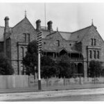 Image: A large, three-storey mid-nineteenth century bluestone building fronted by a dirt street. A sign reading ‘Prince Alfred Sailors’ Home, 1871’ is visible above the front entrance