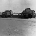 Image: two brick buildings with decorative verandahs which serve as entranceways to a railway station.