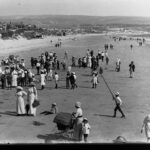 Image: People on a beach with houses and hills in the background.