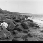 Image: View of a rocky coastline with a young girl clambering over rocks and cliffs in the background