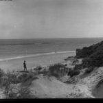 Image: Man on a beach with sand dunes in the foreground.