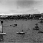 Image: View of boats in the water with crowds of people on the beach in the background