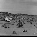 Image: People on a beach sheltering under umbrellas and tents