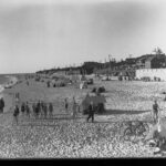 Image: People on a beach in swimsuits and sheltering from the sun under tents.