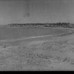 Image: View of a bay with sand dunes in the the foreground and a cliff in the background