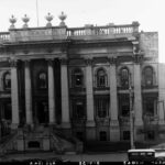 Image: A large rectangular building with two storeys and numerous columns in the Greek revival style