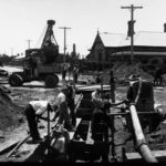 Image: men working on pipes in ditch cut into dirt road