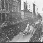 Image: parade of floral floats on street with crowds of people watching.