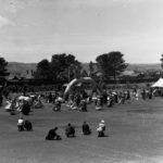 Image: group of people in nineteenth century costume around old arch-shaped tree