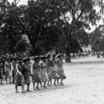 Image: Two lines of girl guides marching in a national park with tall trees in the background