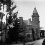 Image: A large, two-storey brick and stone building with a central tower