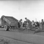 Image: Black and white photo of a drag box being used to spread hotmix (bituminous concrete), this method was a cheap way to provide a smooth surface, 10 November 1937.