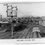 Image: a view of a busy railway yard with a number of parked carriages on a series of tracks. In the background are a series of curved roof buildings.