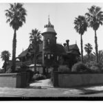 Image: A large, two-storey stone mansion with a cylindrical turret comprising one corner of the structure