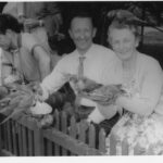 Image: a man and woman looking at camera while feeding pigeons