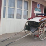 Image: Colour photo of a restored antique horse drawn cart, with a building behind.