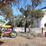 Image: Colour photo of a museum sign on the side of a road, silos in the background.