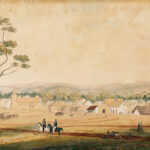 Image: a watercolour painting of two men riding through a field which backs on to a row of small wooden cottages and a small church, all behind a wooden fence.