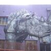 Image: blue and purple mural of a rhinoceros on a brick wall