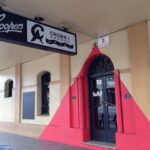 Image: beige building with red triangle over front door, with neon sign hanging above