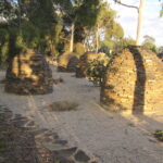 Image: Five large dome-shaped stone structures in a gravel-filled garden bed sit next to a busy road.