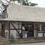 Image: A two-storey building with white walls interrupted at intervals with straight wooden beams