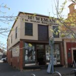 Image: A two-storey building with brick first floor and corrugated metal second floor. The words ‘Hy. Weman, Sail Maker, Ship Chandler’ are painted on the building shop front