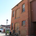 Image: A plain rectangular two-storey brick building with a large double-door loading bay on each floor