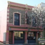 Image: A two-storey stone building with alternating pink and cream-coloured quoining