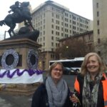 Image: two women stand in front of decorated statue of horse and rider