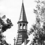 Image: A tower roof with finial and decorative stone arches.