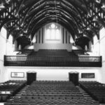 Image: The interior of a large hall with a hammerbeam roof and tiered seating on two levels.