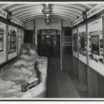 Image: The interior of a train carriage containing a railway model, and walls lined with information panels about railways