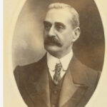 Image: Portrait photograph of a man in an oval frame wearing a suit and tie.