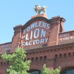 Image: Lion sculpture on top of red brick parapet baring signage 'Fowler's Lion Factory'