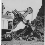 Image: two men operating large machinery inf fron of pile of boulders