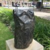 Crumpled bronze bag on plinth with grass and plants nearby