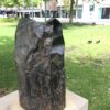 Crumpled bronze bag on plinth with grass and plants nearby