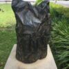 Crumpled bronze bag on plinth with grass and plants nearby