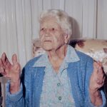 Image: elderly caucasian woman holds up her hands as she retells a story