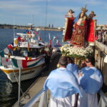 Image: A group of people watch men in Catholic vestments carry an effigy of the Madonna and Child to a motorboat moored at a wharf