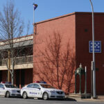 Image: Large red brick building on street corner with fountain and two police cars in front