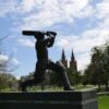 Image: Bronze statue of man with cricket bat with buildings in background