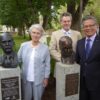 Image: Three people standing with two bronze busts